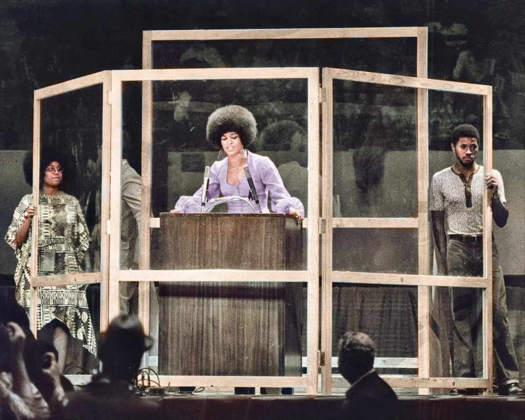 Angela Davis stands behind bulletproof glass panels while speaking at Madison Square Garden