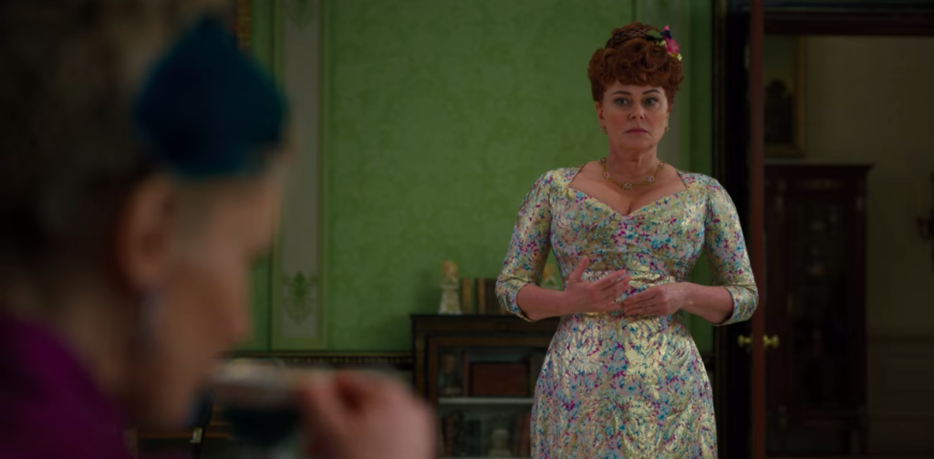 Mrs. Featherington standing in a very, very colorful dress.